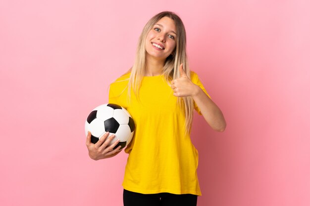 Young football player woman isolated on pink wall giving a thumbs up gesture