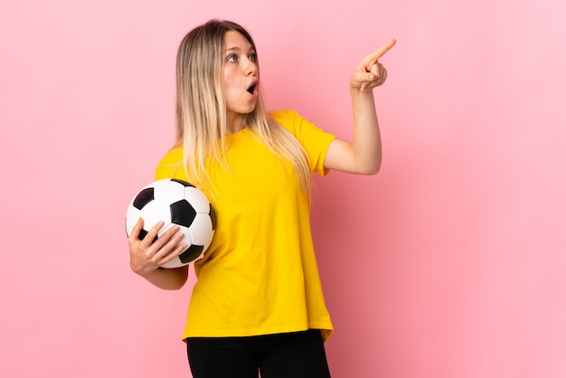 멀리 가리키는 분홍색 벽에 고립 된 젊은 축구 선수 여자
