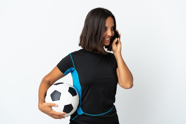 Young football player woman isolated on white keeping a conversation with the mobile phone with someone