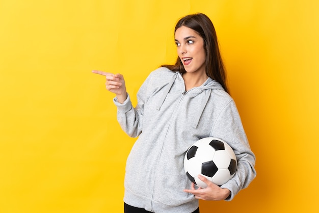 Young football player woman isolated on yellow background pointing finger to the side and presenting a product