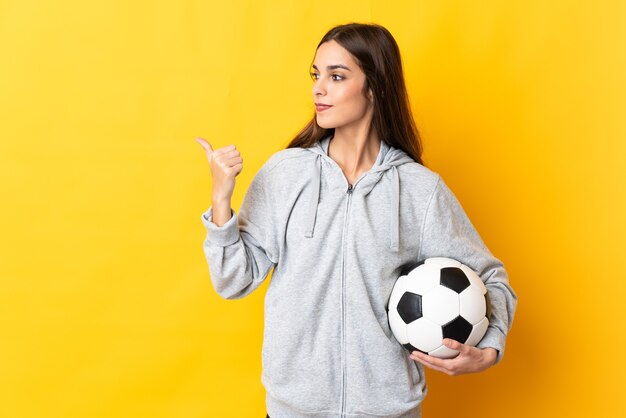 Young football player woman isolated on yellow background pointing to the side to present a product