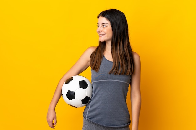 Young football player woman isolated on yellow looking side