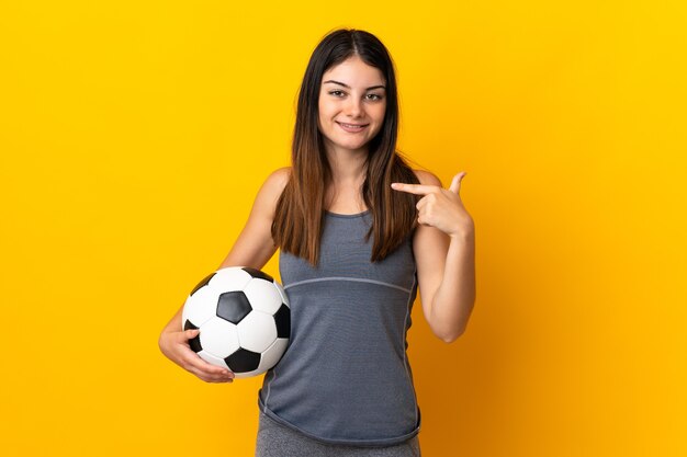 親指を立てるジェスチャーを与える黄色の壁に分離された若いサッカー選手の女性