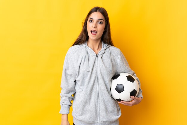 Young football player woman isolated on yellow wall with surprise facial expression