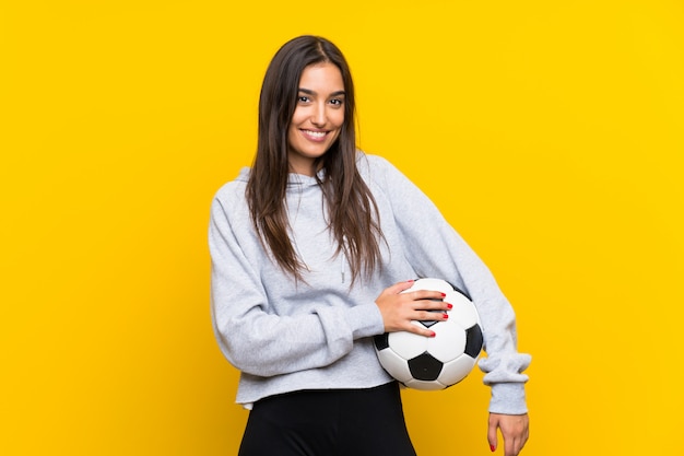 Молодая женщина футболиста над изолированной желтой стеной