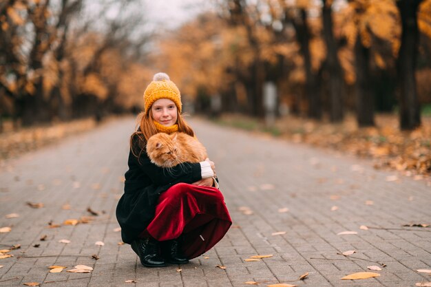 young freckles girl with lovely kitten on her knees posing in valley in autumn park.