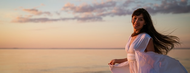 Young free woman running in white dress near the sea at sunset