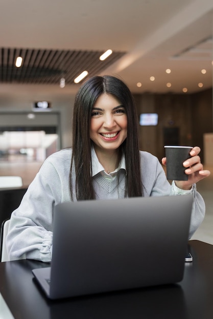 A young freelance woman drinks coffee while working at a laptop in a cafe