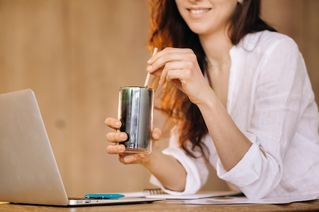 A young freelance woman with a cocktail in her hands at her workplace at work
