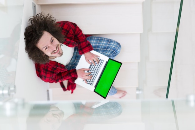 young freelancer in bathrobe working from home using laptop computer while sitting on stairs