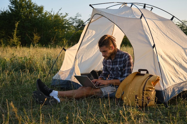 Молодой фрилансер сидит в лагере Удаленная работа на свежем воздухе летом на закате