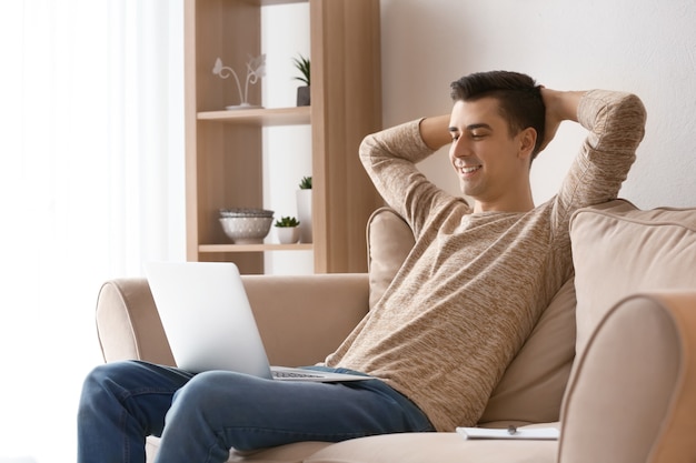 Young freelancer with laptop relaxing on sofa at home