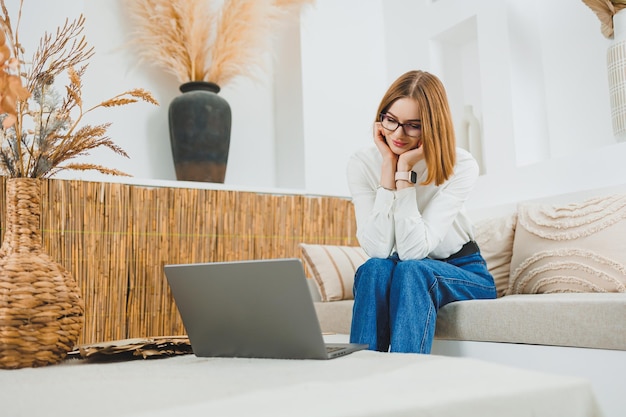 Foto giovane donna freelance seduta sul divano e che lavora al portatile che guarda film sul portatile che studia che scrive blog che si rilassa e che chatta online
