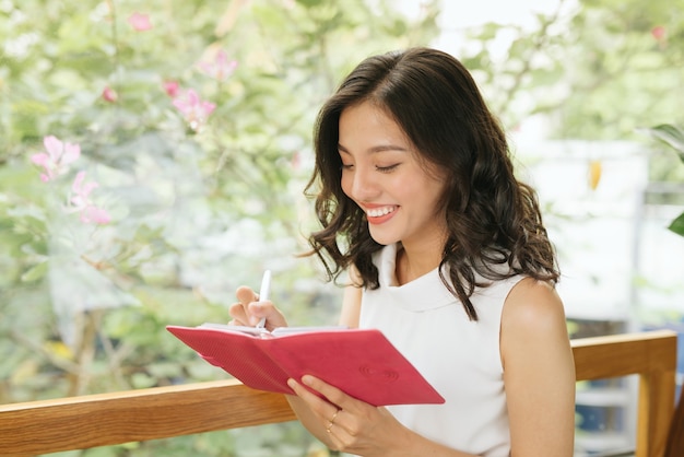 Young freelancer woman writting plans in notebook at the table in modern interior cafe