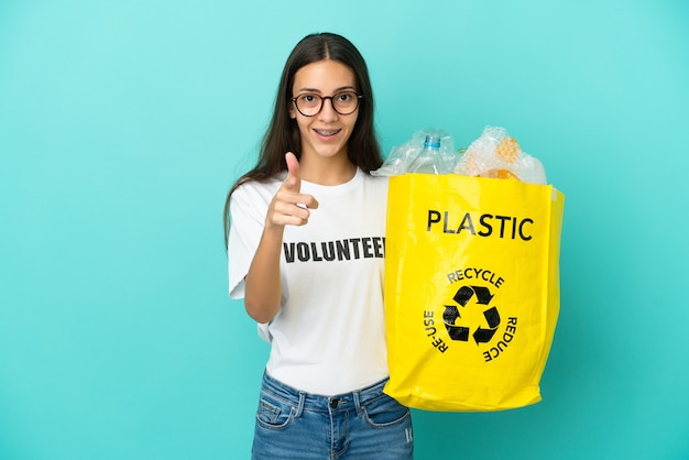 Foto giovane ragazza francese con in mano una borsa piena di bottiglie di plastica da riciclare sorpresa e puntata davanti