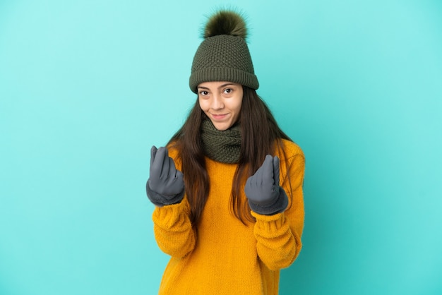 Foto giovane ragazza francese isolata su sfondo blu con cappello invernale che fa gesto di soldi