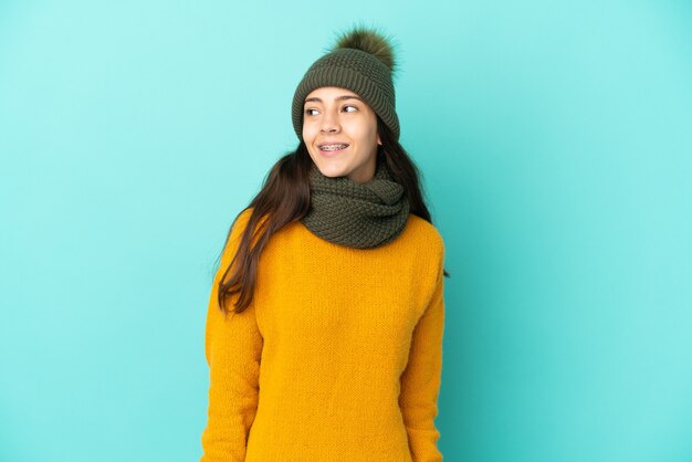Young French girl isolated on blue background with winter hat thinking an idea while looking up