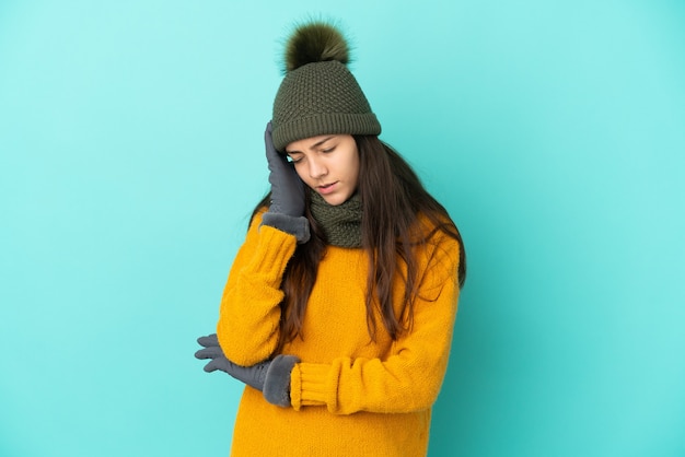 Young French girl isolated on blue background with winter hat with headache