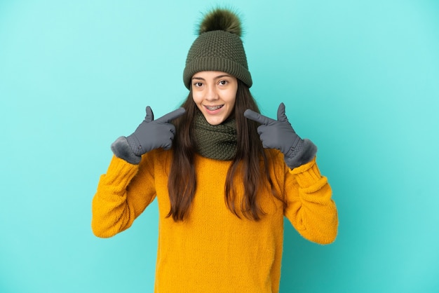 Молодая французская девушка изолирована на синем фоне с зимней шапкой, показывая жест рукой вверх