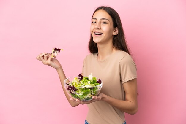 Молодая французская девушка изолирована на розовом фоне, держа миску салата с счастливым выражением лица