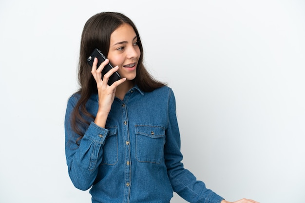 Young French girl isolated on white background keeping a conversation with the mobile phone with someone