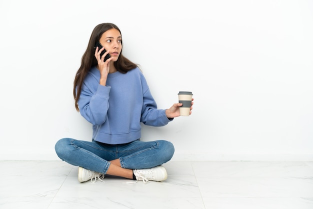 Young French girl sitting on the floor holding coffee to take away and a mobile