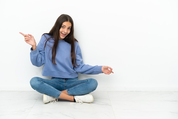 Young French girl sitting on the floor pointing finger to the laterals and happy