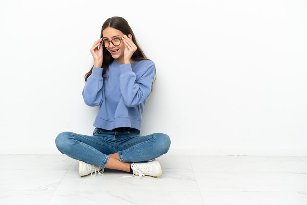 Young French girl sitting on the floor with glasses and surprised