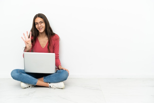 Giovane ragazza francese seduta sul pavimento con il suo laptop felice e contando quattro con le dita