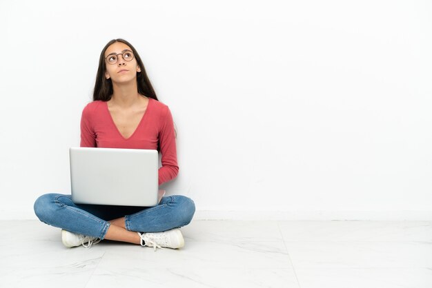 Young French girl sitting on the floor with her laptop and looking up