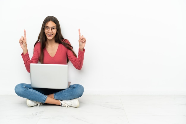 Young French girl sitting on the floor with her laptop pointing up a great idea