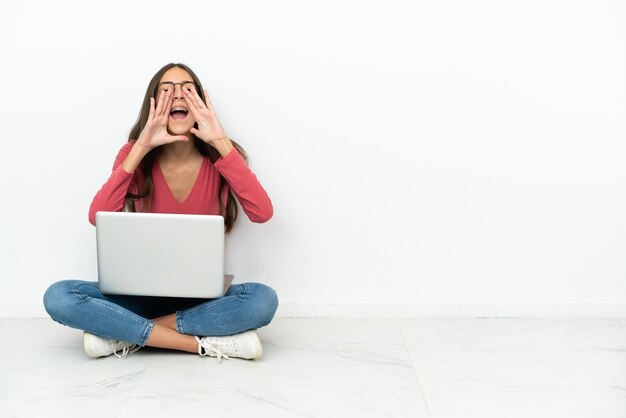 Young French girl sitting on the floor with her laptop shouting and announcing something
