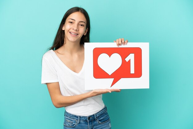 Young French woman isolated on blue background holding a placard with Like icon with happy expression