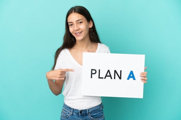 Young French woman isolated on blue background holding a placard with the message PLAN A and  pointing it