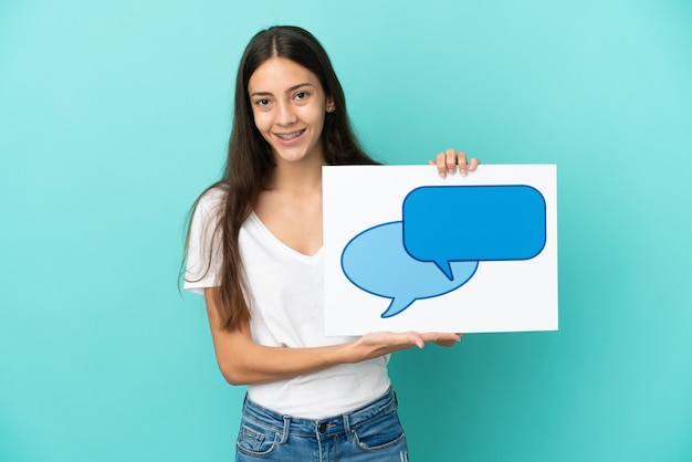 Young French woman isolated on blue background holding a placard with speech bubble icon with happy expression