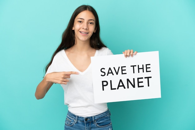 Молодая француженка изолирована на синем фоне, держа плакат с текстом «Спасите планету» и указывая на него