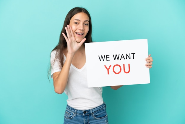 Young French woman isolated on blue background holding We Want You board and shouting