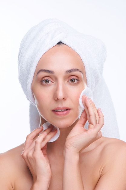 Young fresh beautiful woman with cotton pads looking at you while applying moisturizing lotion on face in isolation