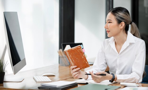 Young friendly asian woman working on document and analyzing weekly schedule in her notebook