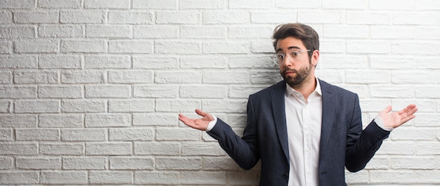 Young friendly business man doubting and shrugging shoulders, concept of indecision and insecurity, uncertain about something