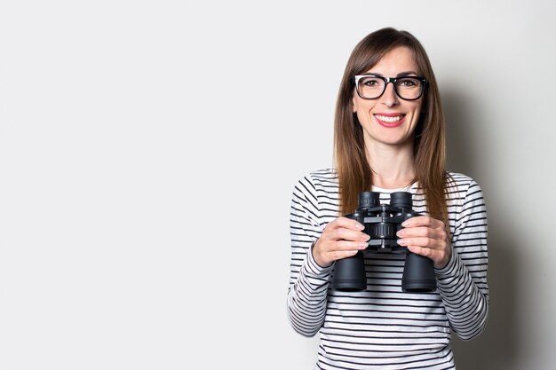 La giovane ragazza amichevole in una maglietta tiene il binocolo su uno spazio luminoso.