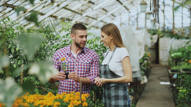 Young friendly woman gardener talking to customer and giving him advice while working in garden