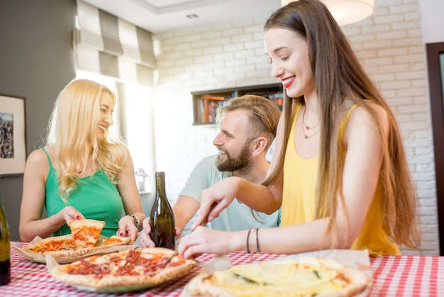 Giovani amici vestiti casualmente con magliette colorate pranzando con pizza e birra a casa