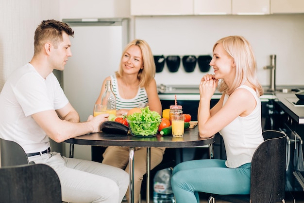 Young friends having party at home, eating pizza, drinking fruit juice and smiling. The cheerful company of youth people resting in kitchen. Friendship, people and food concept.