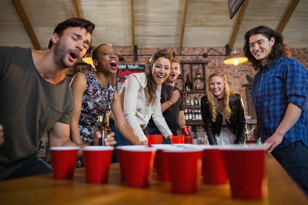 young friends playing beer pong game in bar