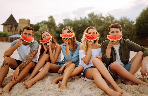 Молодые друзья отдыхают на пляже и едят арбуз Люди летний образ жизни