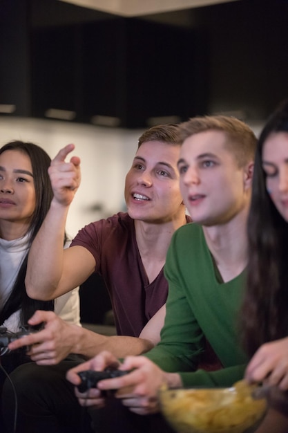 Young friends sitting on the sofa young men holding a joystick and women eating chips