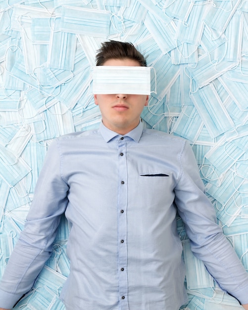 Young frustrated guy with a mask on his face lies on scattered masks. Concept of stress during a pandemic and crisis in the world.