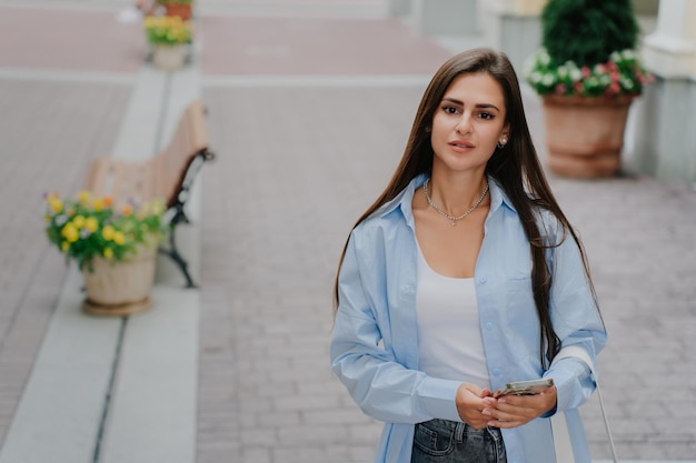 Young frustrated woman holding phone staring aside received\
message makes decision what to do cute hispanic girl hesitating\
walking aside pretty thoughtful female in casual decides to make a\
call