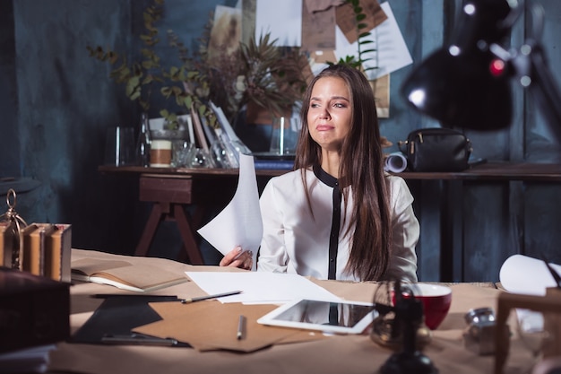Молодая разочарованная женщина, работающая на чердаке дома или за офисным столом перед ноутбуком, страдает от хронических ежедневных головных болей